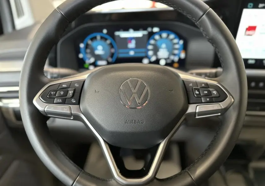 Vue rapprochée du volant multifonction en similicuir noir du Volkswagen Transporter T7 avec tableau de bord numérique en arrière-plan.