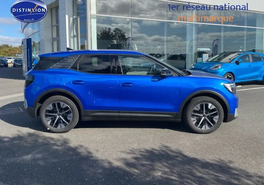 Ford Explorer électrique bleu Premium My Mind vu de profil côté gauche, stationné devant un bâtiment vitré.