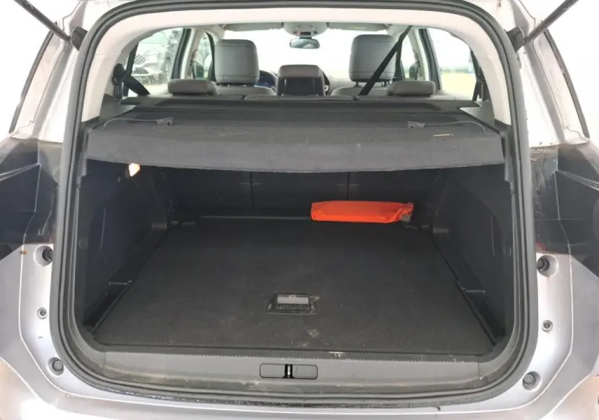 Coffre ouvert vu de l'arrière d'un Citroën C5 Aircross gris Artense avec cache-bagages et trousse de secours orange.