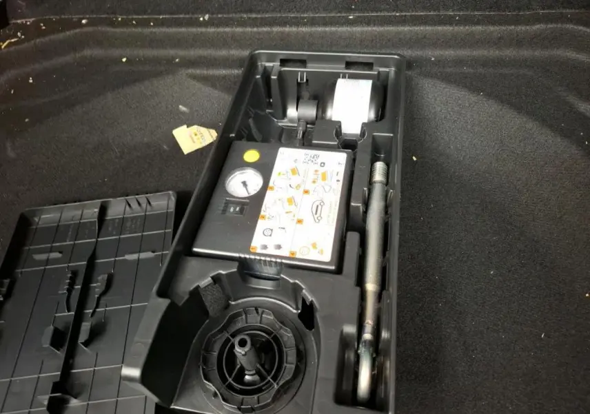 Coffre ouvert d’un Citroën C5 Aircross gris, montrant le kit de dépannage pneumatique rangé dans un compartiment noir.