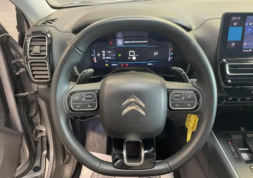 Vue intérieure centrée sur le volant cuir noir du Citroën C5 Aircross gris avec tableau de bord numérique et écran tactile.