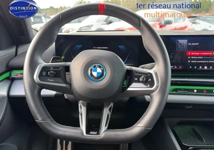 Vue intérieure centrée sur le volant sport noir avec bande rouge, tableau de bord digital et inserts verts de la BMW Série 5 i5 M60 2024.