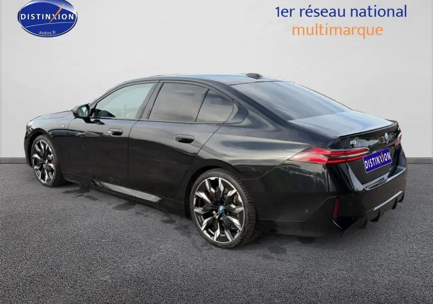 BMW Série 5 i5 M60 noir vue 3/4 arrière droit avec jantes alu bicolores et feux arrière LED allumés.