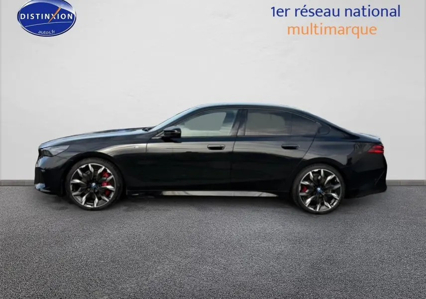 BMW Série 5 i5 M60 noire vue de profil côté gauche avec jantes alu bicolores et étriers rouges visibles.