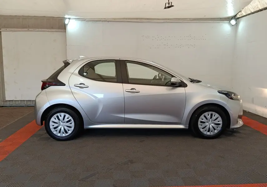 Profil droit d'une Toyota Yaris hybride gris clair 2022, avec jantes standard et lignes dynamiques visibles.