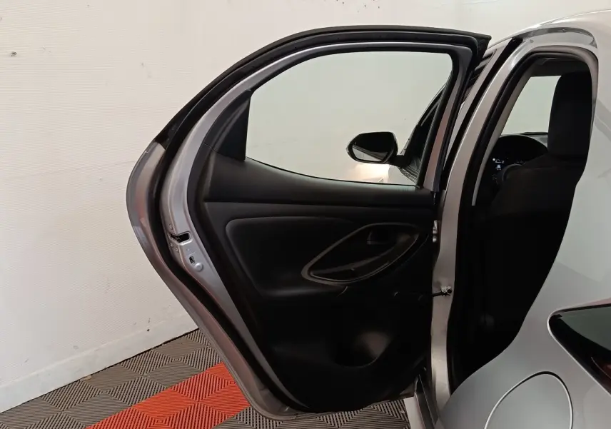 Vue arrière côté gauche de la Toyota Yaris hybride gris clair avec porte arrière ouverte et intérieur noir visible.