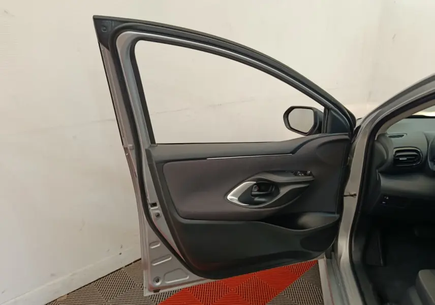 Porte avant gauche ouverte d'une Toyota Yaris hybride gris clair, montrant la garniture intérieure noire et poignée argentée.