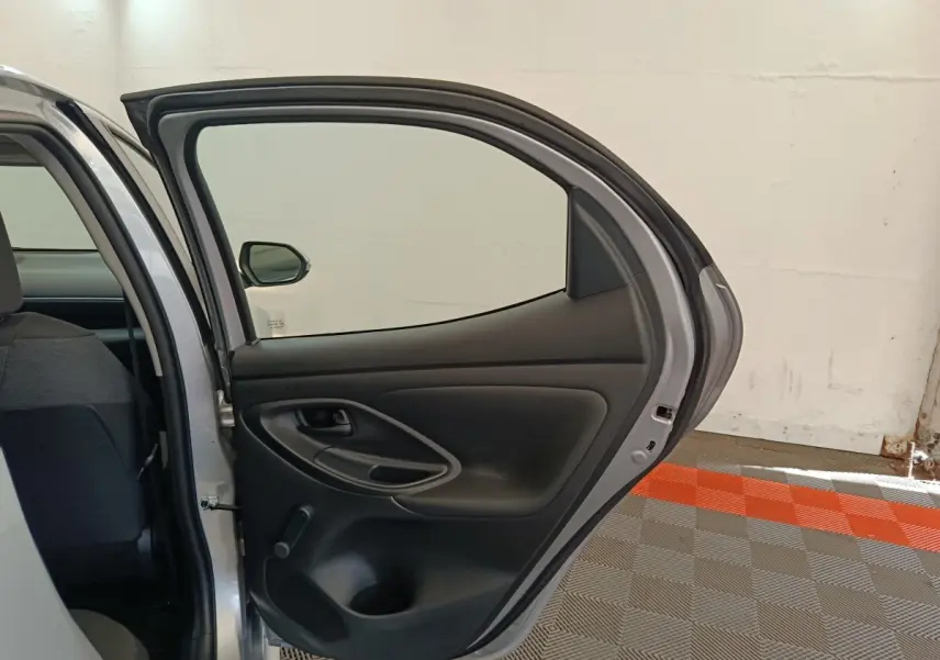Vue intérieure de la porte arrière droite ouverte d'une Toyota Yaris hybride gris clair, montrant la garniture noire et la manivelle de vitre.