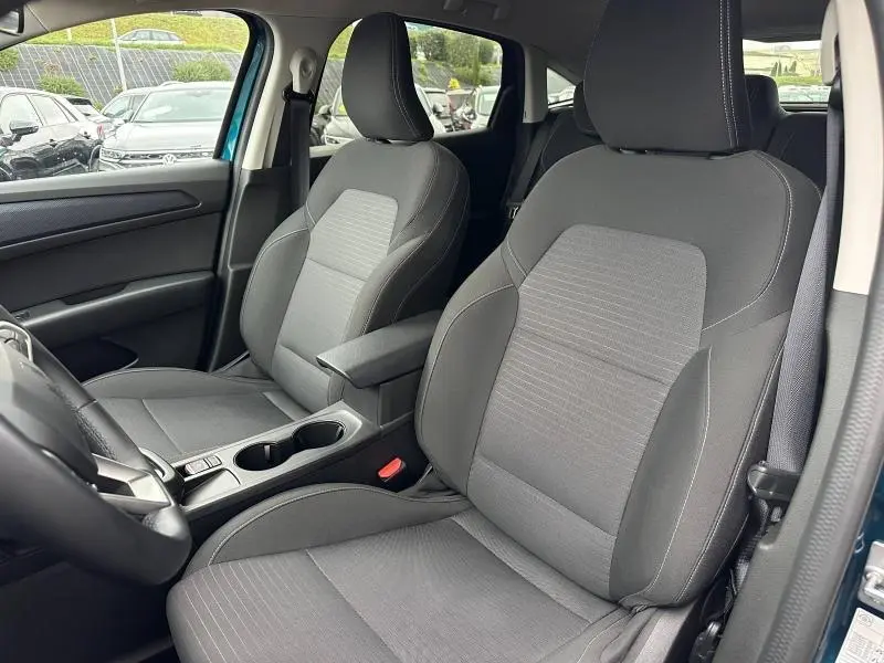 Vue intérieure côté avant droit du Renault Arkana 2025 bleu Zanzibar, montrant les sièges avant en tissu gris et la console centrale.