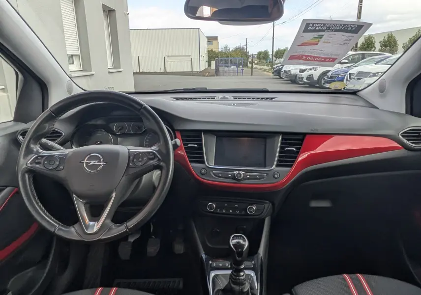 Vue intérieure avant de l'Opel Crossland X 2021, tableau de bord noir avec inserts rouges et sièges tissu noir à bandes rouges.