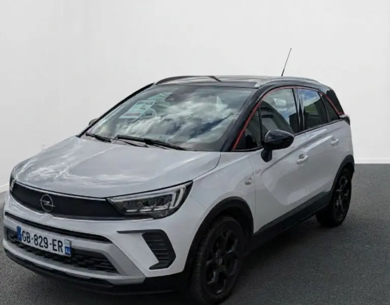 Opel Crossland X blanc en 3/4 avant droit avec toit noir et jantes noires, sur fond neutre intérieur.