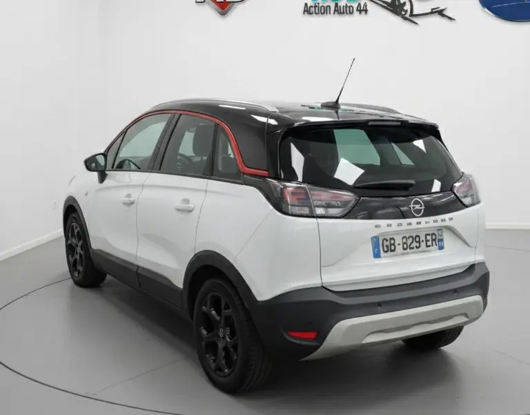 Vue 3/4 arrière droite d'un Opel Crossland X blanc avec toit noir et jantes noires en intérieur studio.