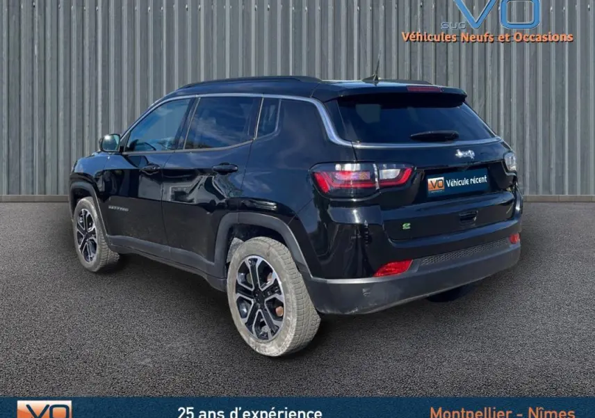 Vue 3/4 arrière droite d'un Jeep Compass noir 2023 avec barres de toit et jantes 18 pouces sur fond industriel.