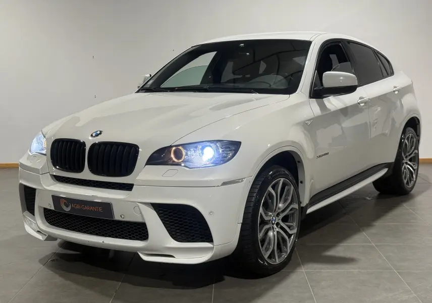 BMW X6 xDrive 40d blanc vue 3/4 avant droit avec phares allumés et jantes M Sport distinctives.