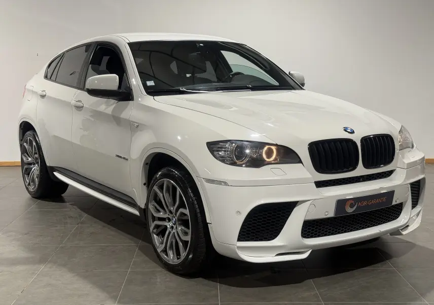 BMW X6 xDrive 40d blanc vue 3/4 avant droit, avec jantes M Sport et phares allumés en intérieur.