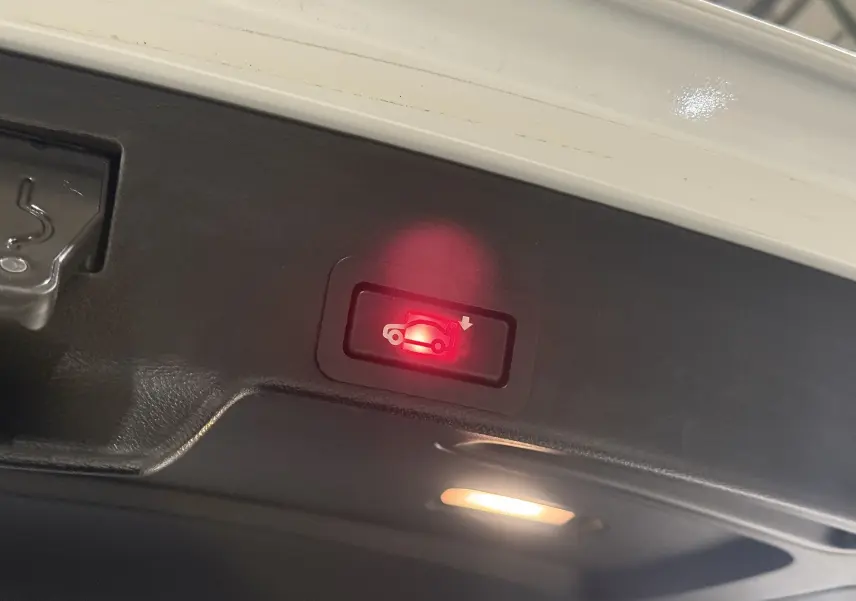 Gros plan sur le bouton lumineux rouge d'ouverture électrique du coffre d'un BMW X6 blanc, version M Sport 2026.