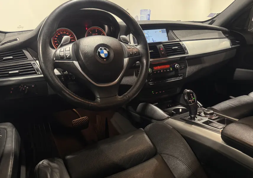 Intérieur BMW X6 xDrive 40d 2026 vu côté conducteur, volant cuir, console centrale avec levier de vitesses automatique.