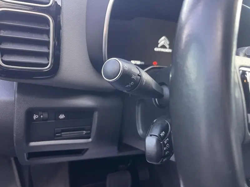 Gros plan sur la commande des phares à gauche du volant dans l'habitacle gris du Citroën C5 Aircross 2021.
