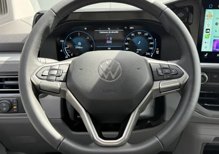 Vue rapprochée du volant multifonction noir du Volkswagen Transporter T7 avec tableau de bord numérique et écran tactile latéral.