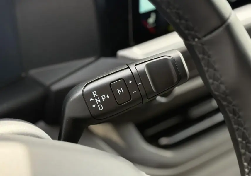 Gros plan sur le levier de vitesses automatique noir à commandes blanches, côté droit du volant du Volkswagen Transporter gris argent.