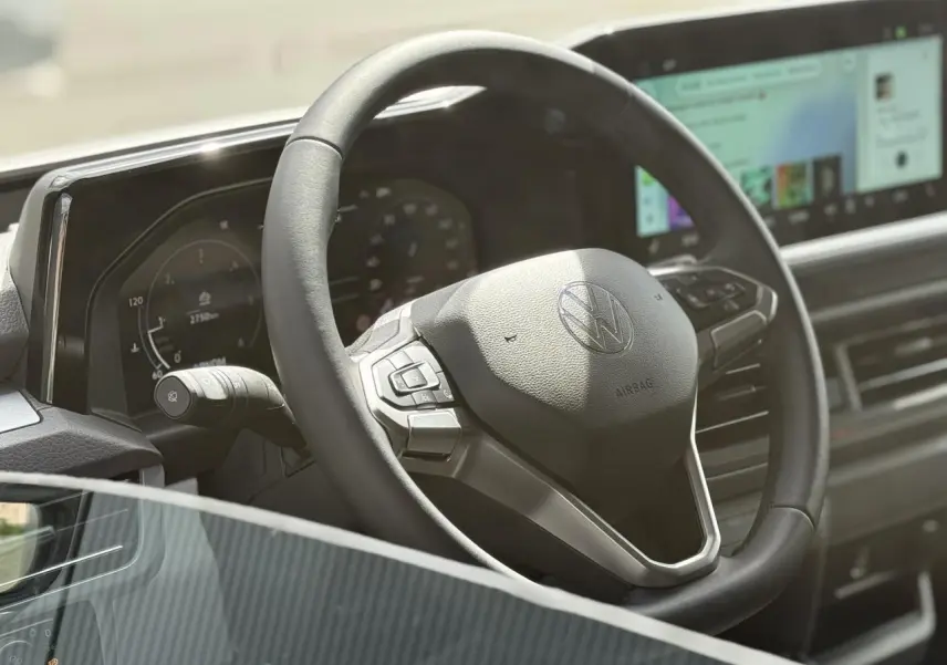 Gros plan sur le volant multifonction noir du Volkswagen Transporter T7 avec tableau de bord digital et écran tactile.