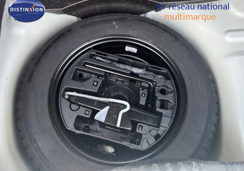 Gros plan sur la roue de secours noire et ses outils dans le coffre d'une Citroën C3 blanche de 2018.