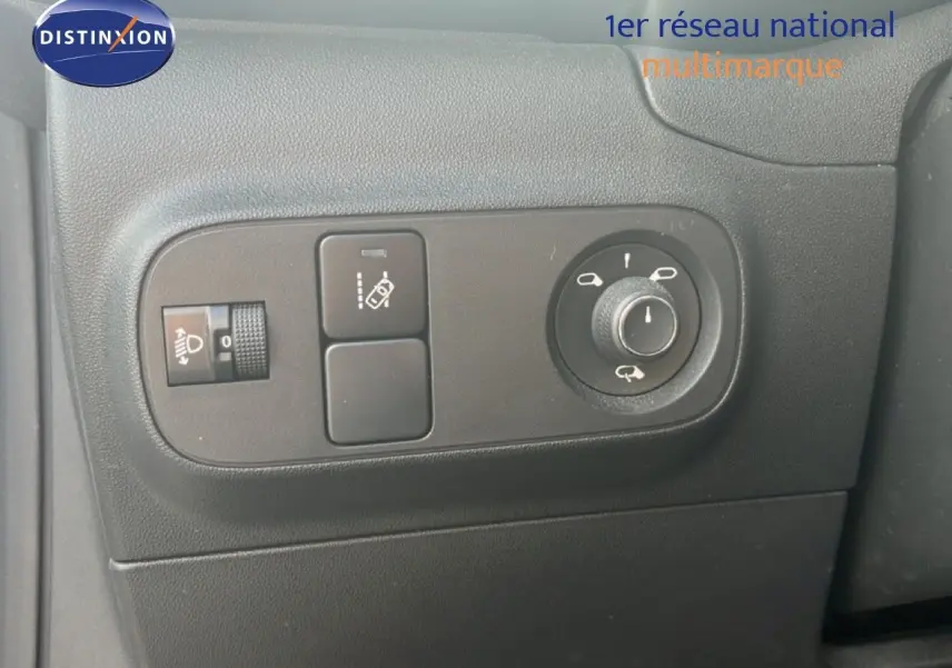 Gros plan sur les commandes de réglage des rétroviseurs et des phares à gauche du tableau de bord d'une Citroën C3 blanche.