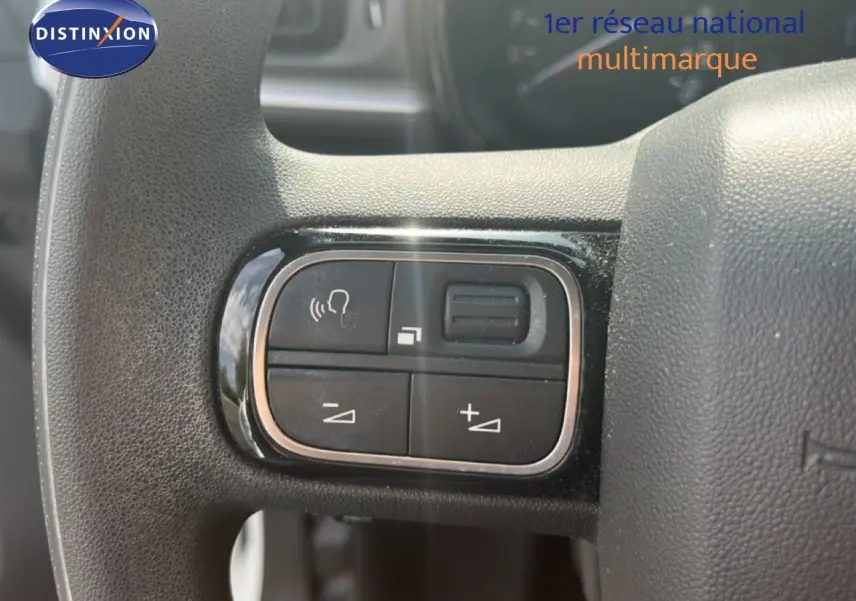Gros plan sur les commandes de volume et téléphone intégrées au volant noir d'une Citroën C3 blanche de 2018.