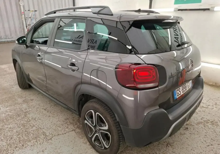 Vue 3/4 arrière droite d'un Citroën C3 Aircross gris foncé avec barres de toit noir brillant et feux arrière LED.