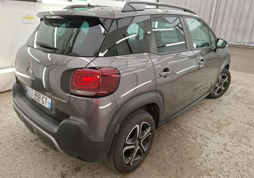 Vue 3/4 arrière droit d'un Citroën C3 Aircross gris foncé avec barres de toit noires et feux arrière LED.