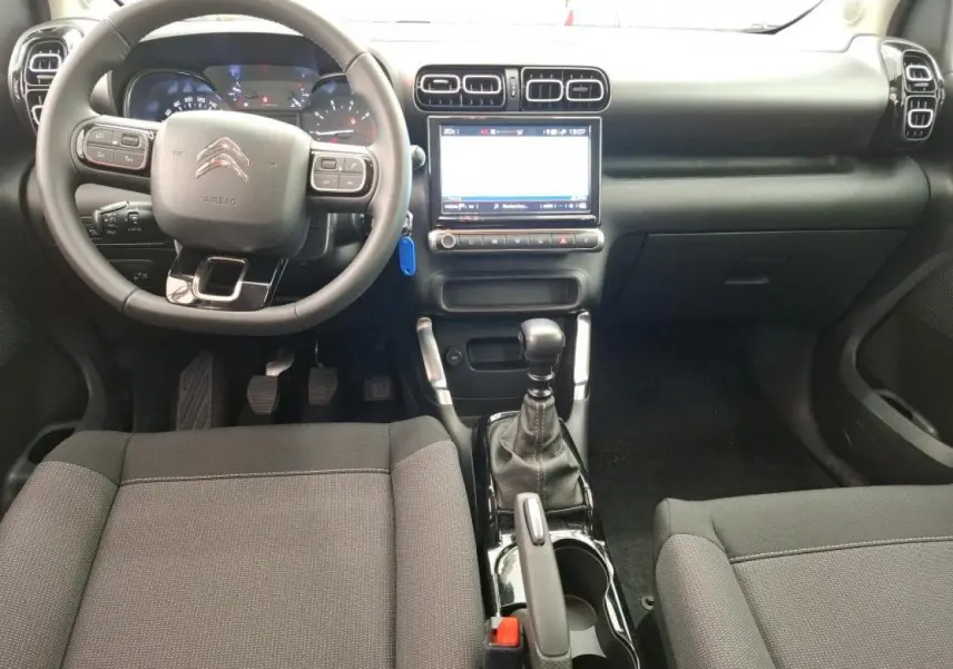 Vue intérieure avant du Citroën C3 Aircross 2023 avec tableau de bord noir, volant multifonction et console centrale brillante.
