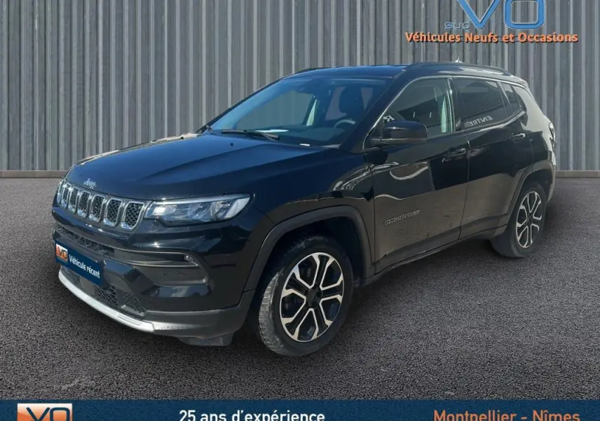 Jeep Compass noir en 3/4 avant droit, avec barres de toit et jantes 18 pouces visibles sur fond urbain.