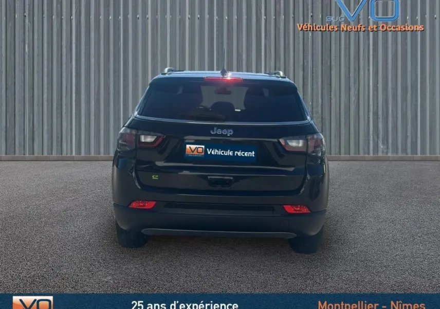 Vue arrière d'un Jeep Compass noir 2023 avec feux arrière LED et barres de toit visibles sur fond industriel.