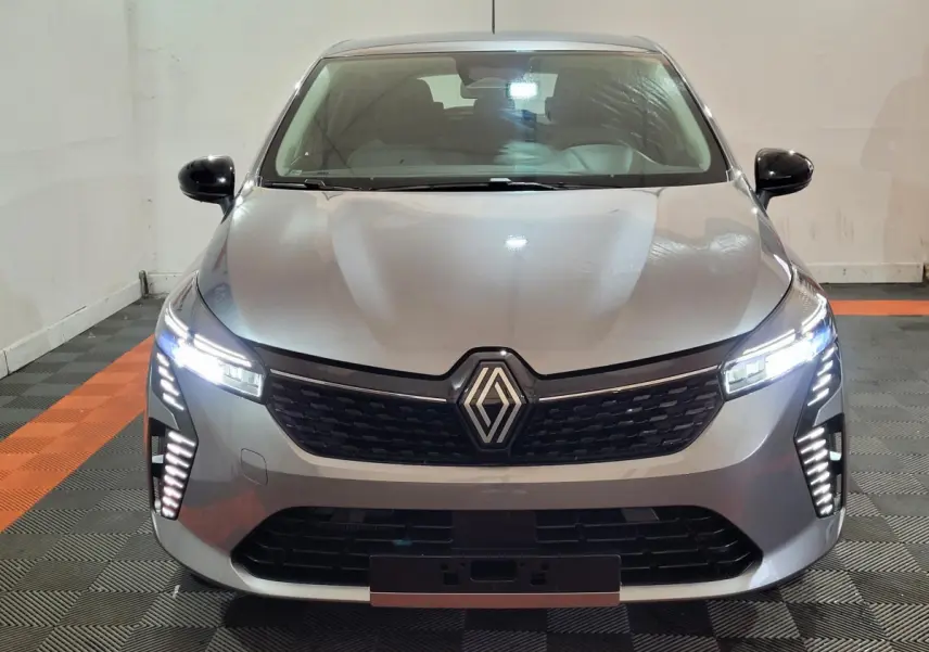 Vue frontale d'une Renault Clio gris foncé 2025 avec phares à LED allumés et calandre noire distinctive.