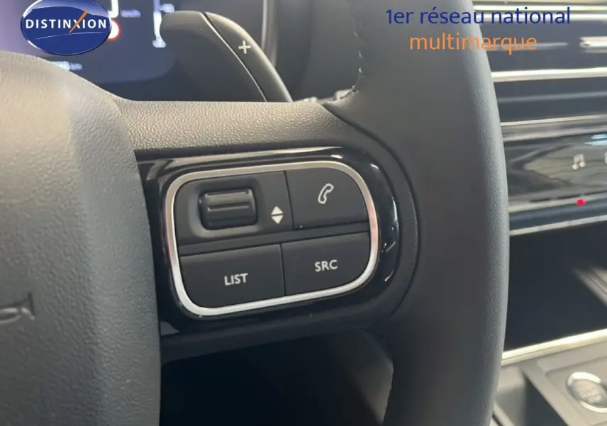 Gros plan sur les commandes au volant noir du Citroën C5 Aircross 2025 hybride, avec tableau de bord en arrière-plan.