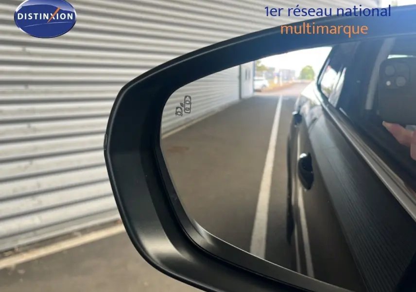Rétroviseur côté droit d'une Citroën C5 Aircross noire métal 2025, avec reflet de la carrosserie et main tenant un téléphone.