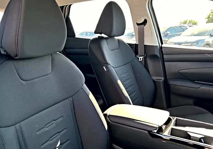 Vue intérieure côté droit des sièges avant noirs du Hyundai Tucson 2026 avec accoudoir central et ceinture de sécurité.