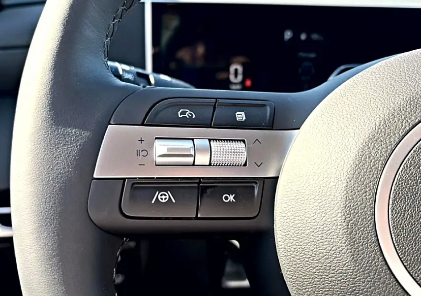 Gros plan sur les commandes gauche du volant cuir noir du Hyundai Tucson 2026 hybride, avec molette argentée.