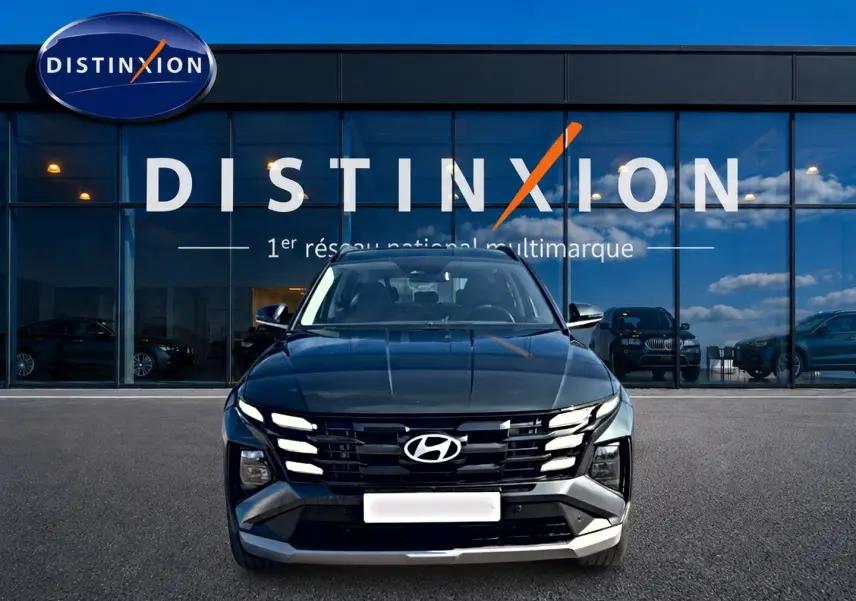 Vue avant d'un Hyundai Tucson vert 2026 avec calandre noire et feux LED distinctifs, devant une vitrine Distinxion.