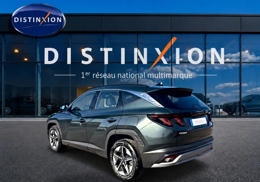 Vue 3/4 arrière gauche d'un Hyundai Tucson vert 2026 devant une vitrine Distinxion, jantes alu 18 pouces visibles.