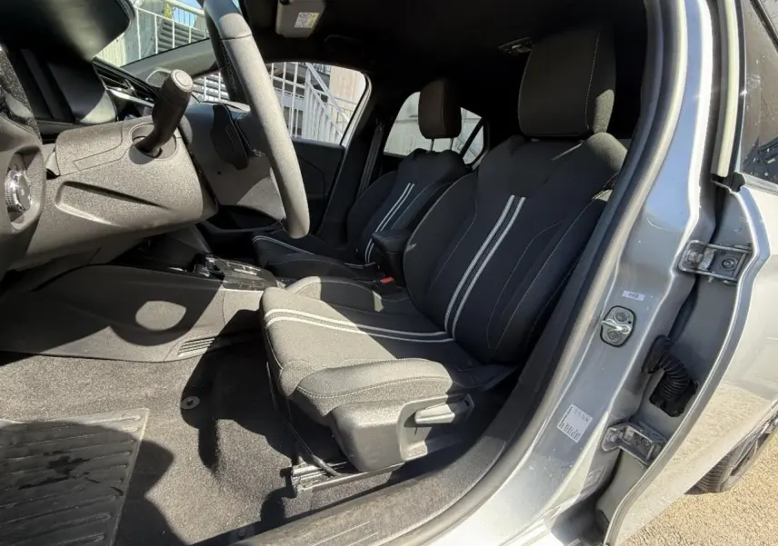 Vue intérieure côté conducteur de l’Opel Corsa 2025 gris graphite, montrant les sièges avant avec surpiqûres blanches et volant.