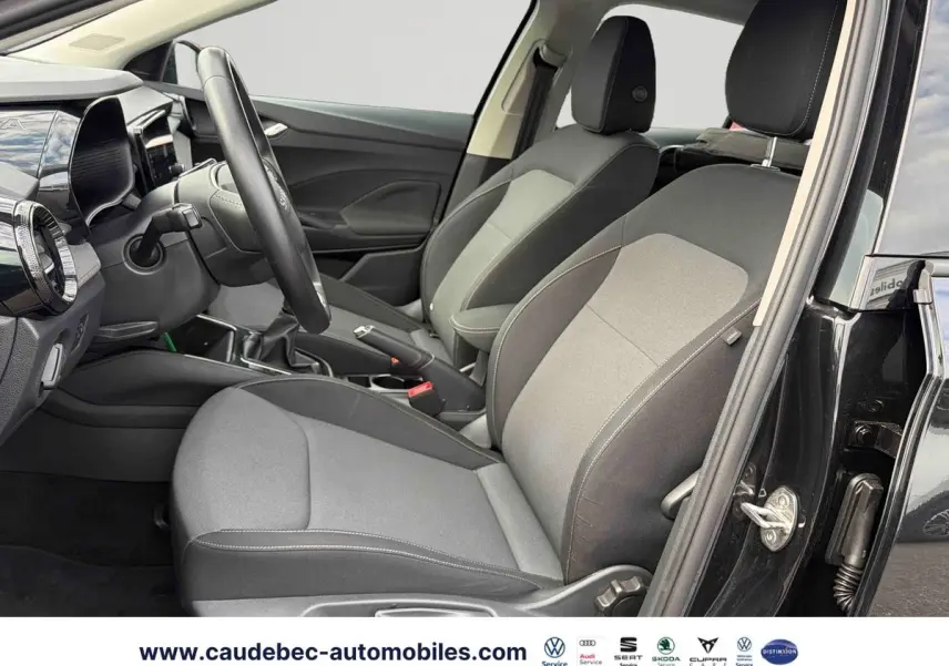 Vue intérieure côté conducteur de la Skoda Fabia noire 2025, sièges tissu gris et volant cuir multifonctions.