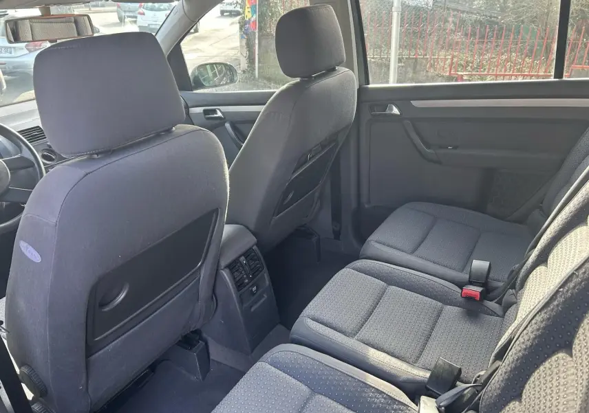 Vue intérieure arrière du Volkswagen Touran gris 2004, montrant les sièges tissu et la console centrale avec aérateurs.