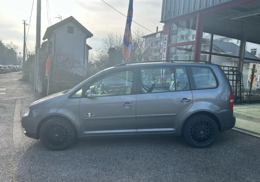 Profil côté gauche d'un Volkswagen Touran gris 2004 avec jantes noires et logo Red Bull sur la porte avant.