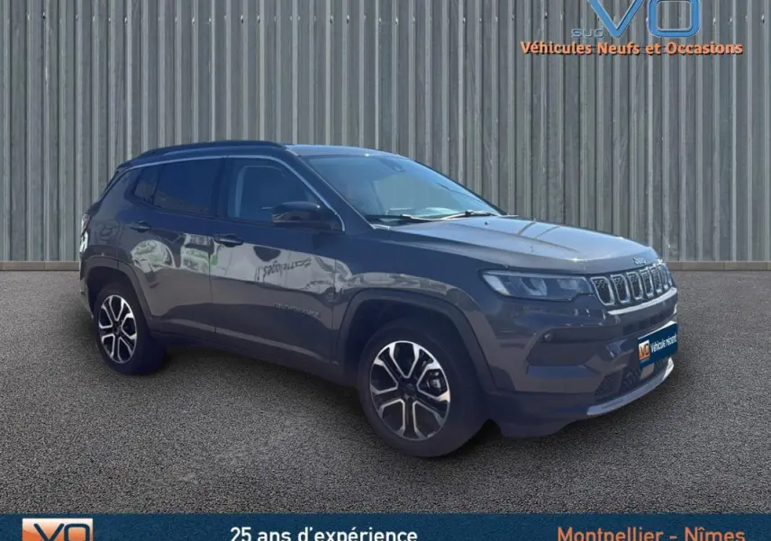 Jeep Compass gris en 3/4 avant droit, avec jantes 18 pouces et barres de toit visibles sur fond urbain.
