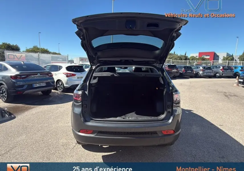 Vue arrière d'un Jeep Compass gris 2023 avec coffre ouvert, stationné en extérieur sous un ciel bleu.