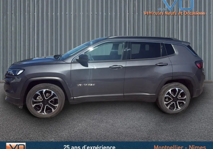 Profil côté gauche d'un Jeep Compass gris 2023 avec jantes 18 pouces et barres de toit visibles sur fond industriel.