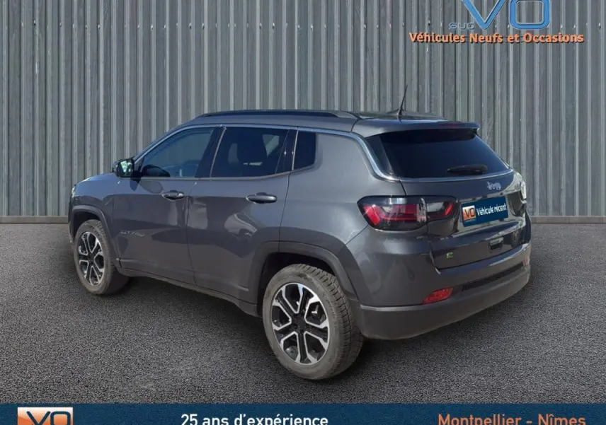 Jeep Compass gris en 3/4 arrière droit, avec barres de toit et jantes 18 pouces visibles sur fond neutre.