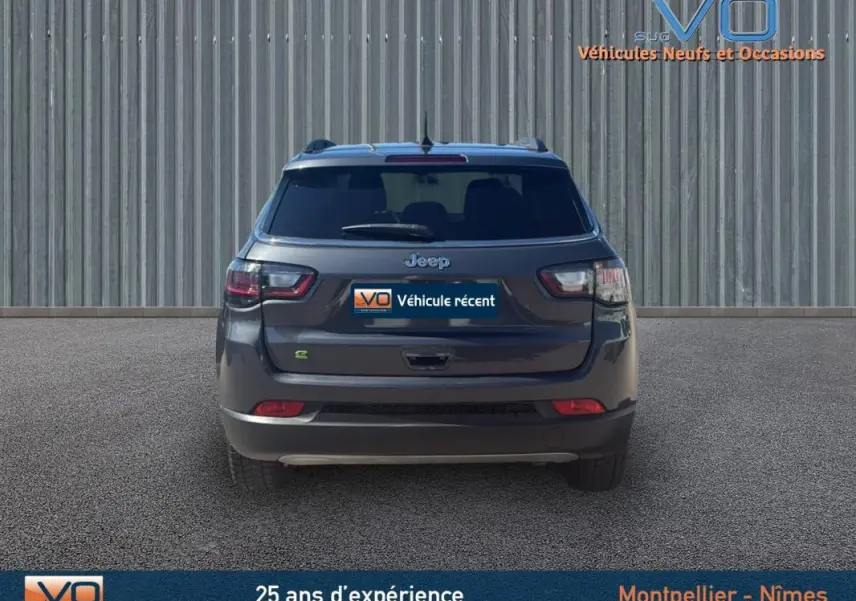 Vue arrière d'un Jeep Compass gris 2023 avec barres de toit et feux arrière LED visibles sur un sol goudronné.