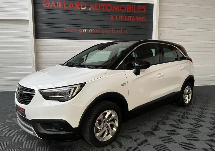 Opel Crossland X blanc vue 3/4 avant droit, toit noir et jantes alliage, stationné en intérieur showroom.
